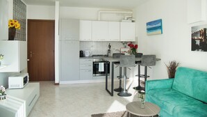 A modern kitchen with white cabinets, a dining area with bar stools, and a teal sofa.