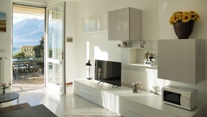 A modern living room with a flat-screen TV, a microwave, and a vase of flowers on a white cabinet.