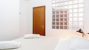 A bedroom with a wooden door, a large window with a grid pattern, and a bed with white linens.