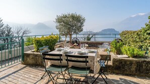 An outdoor dining area with a table set for two, overlooking a body of water and mountains.
