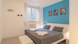 Un dormitorio con cama, ventana con cortinas, radiador y tres adornos florales en la pared.