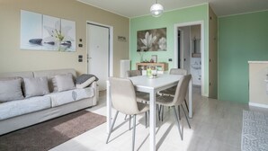 Una sala moderna con sofá, mesa de comedor y sillas. Dos puertas conducen a otras habitaciones.