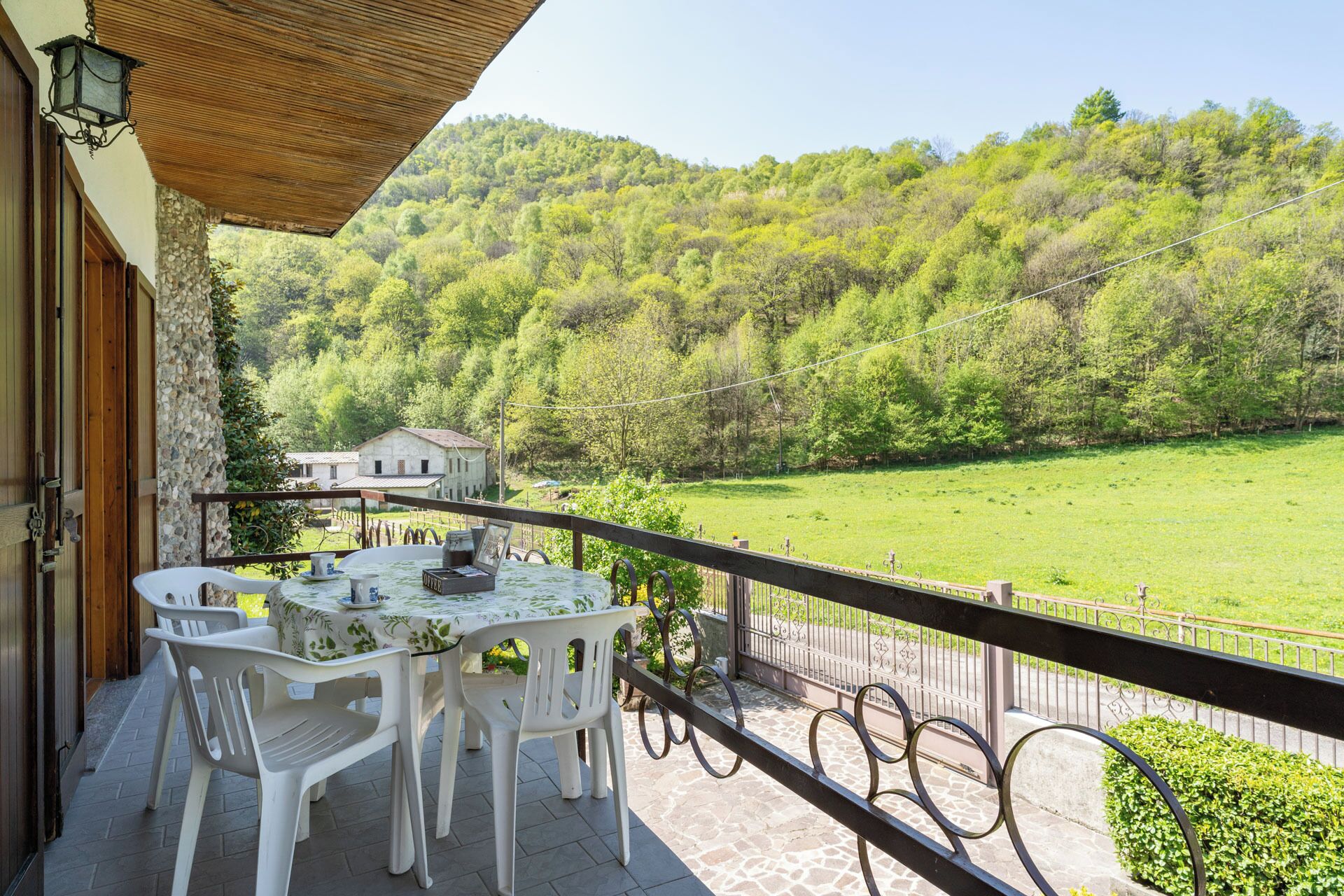 Uma varanda com mesa e cadeiras, com vista para um vale verde e um edifício ao longe.
