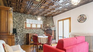 Un salon chaleureux avec une cheminée, un plafond en bois et un coin repas comprenant une table et des chaises.