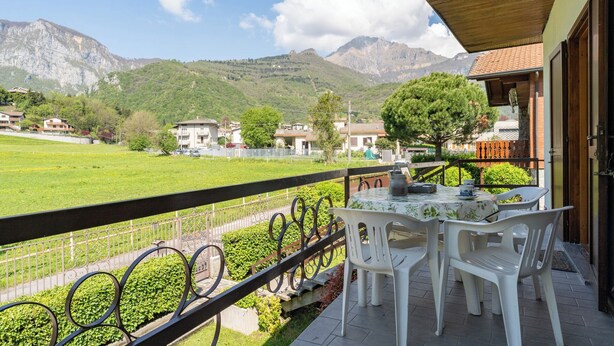 Un balcon avec une table et des chaises, donnant sur un champ verdoyant et des montagnes.