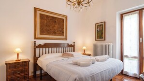 Un lit bien fait, avec une tête de lit en bois, deux tables de chevet avec des lampes, un radiateur et un grand tableau encadré au mur.