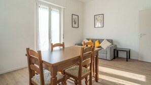 Un comedor con una mesa y sillas de madera, un sofá gris con cojines amarillos, y dos obras de arte enmarcadas en la pared.