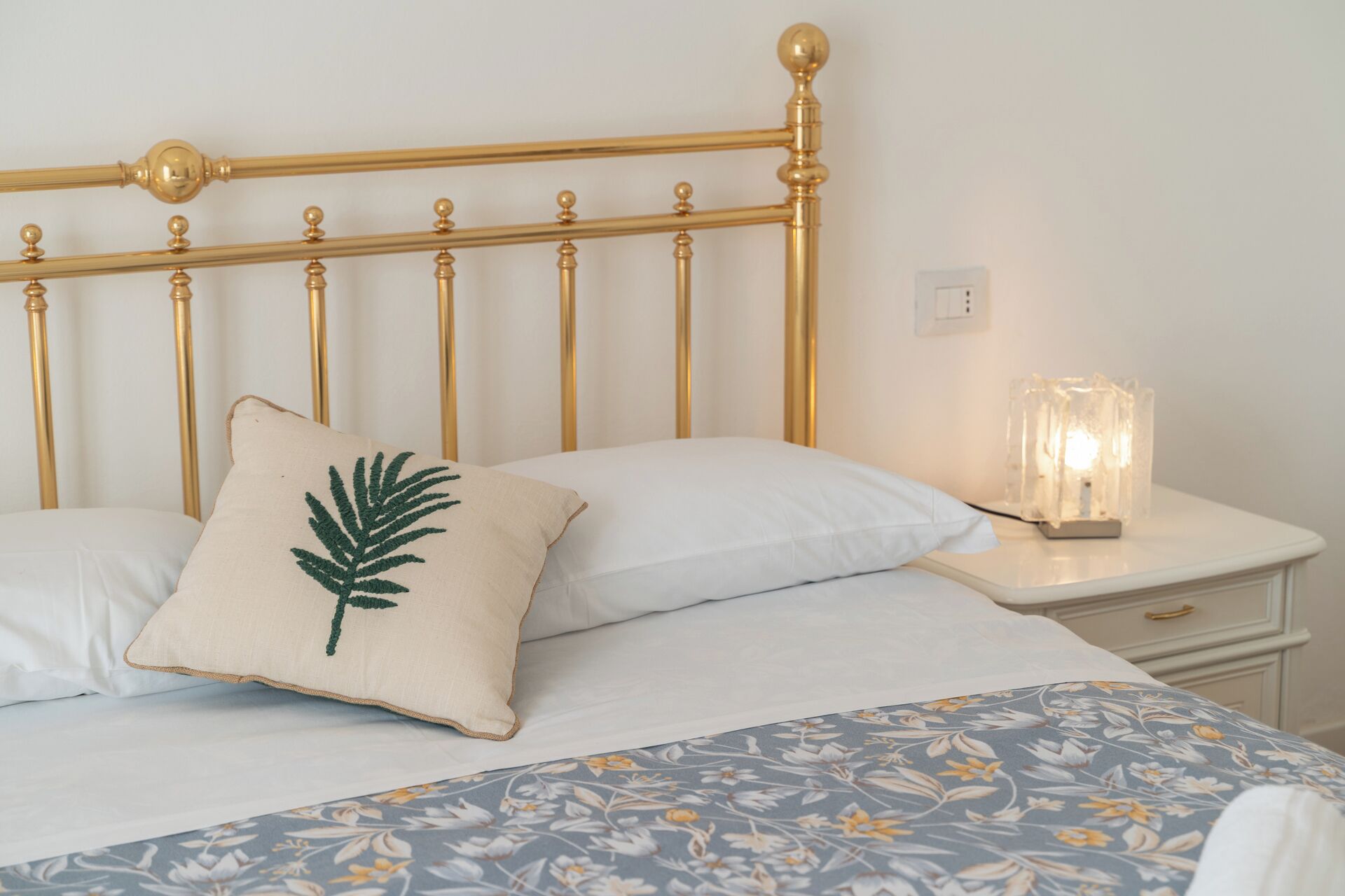 A bed with a gold headboard, white bedding, and a floral-patterned bedspread.