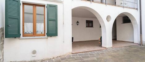 A building with a balcony, stone flooring, and a window with green shutters.