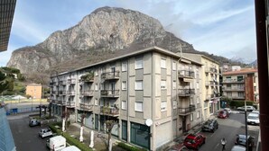 Un edificio residencial de varios pisos con balcones, un estacionamiento y una montaña al fondo.