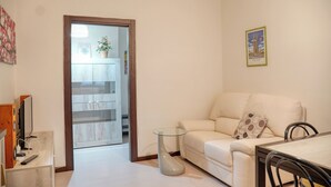Una sala de estar con un sofá, una mesa de centro de vidrio, un televisor y una mesa de comedor con sillas.