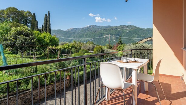 Un balcon avec une table et des chaises, donnant sur un paysage montagneux parsemé de vignobles.