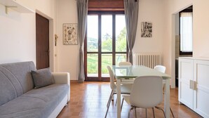 Un espace de vie compact comprenant un canapé, une table à manger avec des chaises, un radiateur et une fenêtre avec des rideaux.