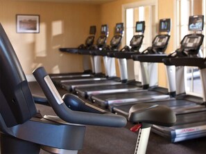 Varias bicicletas estáticas con pantallas digitales, dispuestas en un gimnasio con una pared color crema y una ventana al fondo.