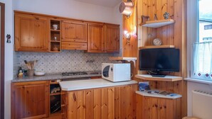 Une cuisine avec des meubles en bois, une cuisinière à gaz, un four à micro-ondes, une télévision et une petite étagère ornée d’objets décoratifs.