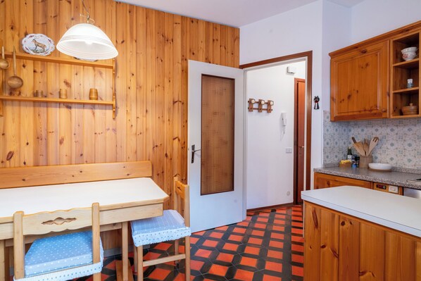 A kitchen with wooden cabinets, a white countertop, and a dining area with a table and bench.