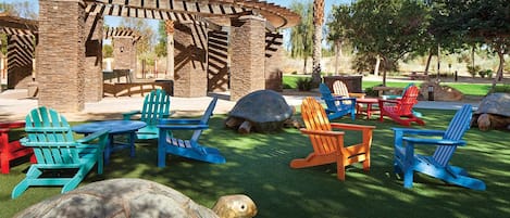 A patio area with Adirondack chairs, a wooden pergola, and a turtle sculpture.