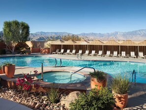 A pool area with a hot tub, lounge chairs, and a mountain view.