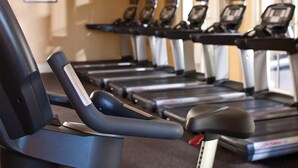 A row of stationary bikes with digital screens, arranged in a gym with a beige wall and a window in the background. - Marriott's Shadow Ridge  One-Bedroom Villa (Palm Desert)