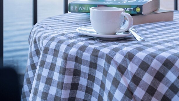 Een balkon met een geruit tafelkleed, een witte kop en een boek getiteld 'The Garden Party' van B. P. Walters.