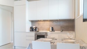 Een moderne keuken met witte kasten, een inbouwoven en een eethoek met een marmeren tafel en stoelen.