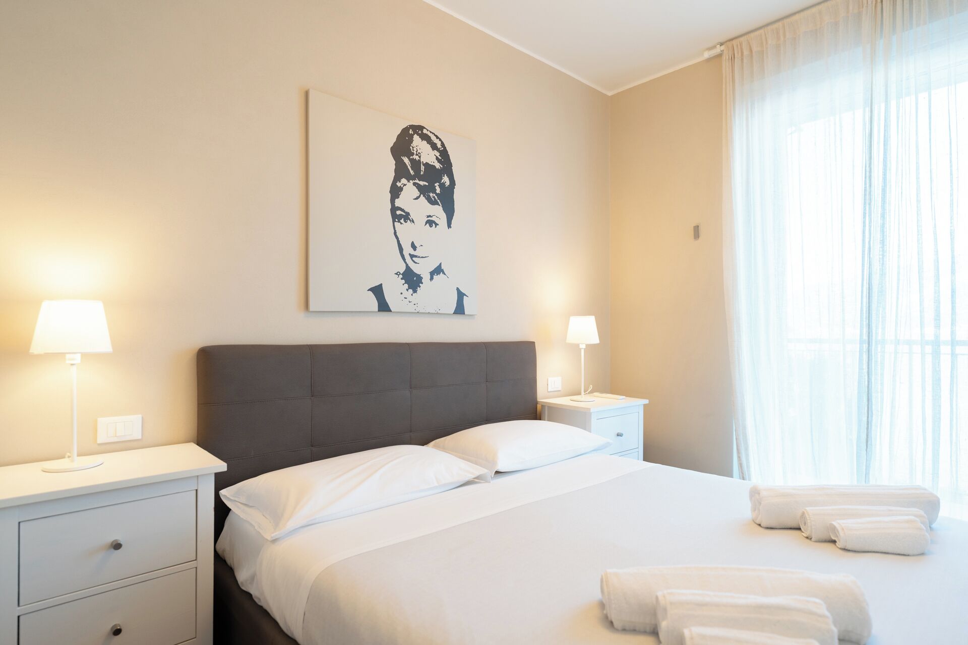 Ein Hotelzimmer mit einem Bett, zwei Nachttischen, einer Lampe und einem Fenster mit Vorhängen.