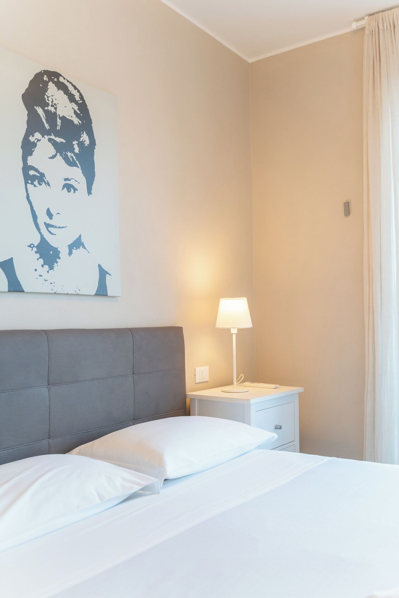 Una camera d'albergo con un letto, un comodino, una lampada e una parete con un ritratto.
