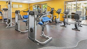 A gym with various exercise machines, a yellow wall, and a large window with a view of buildings outside. - Marriott's Desert Springs Villas | Studio Suite (Palm Desert)