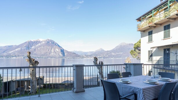 A terrace with a table set for dining, overlooking a lake with mountains in the background.