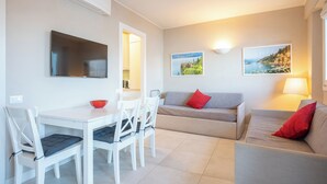 A modern living room with a dining area, featuring a flat-screen TV, a sofa, a table, and chairs.