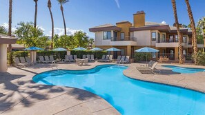 A pool area with lounge chairs and umbrellas, a pool, and a building with balconies.