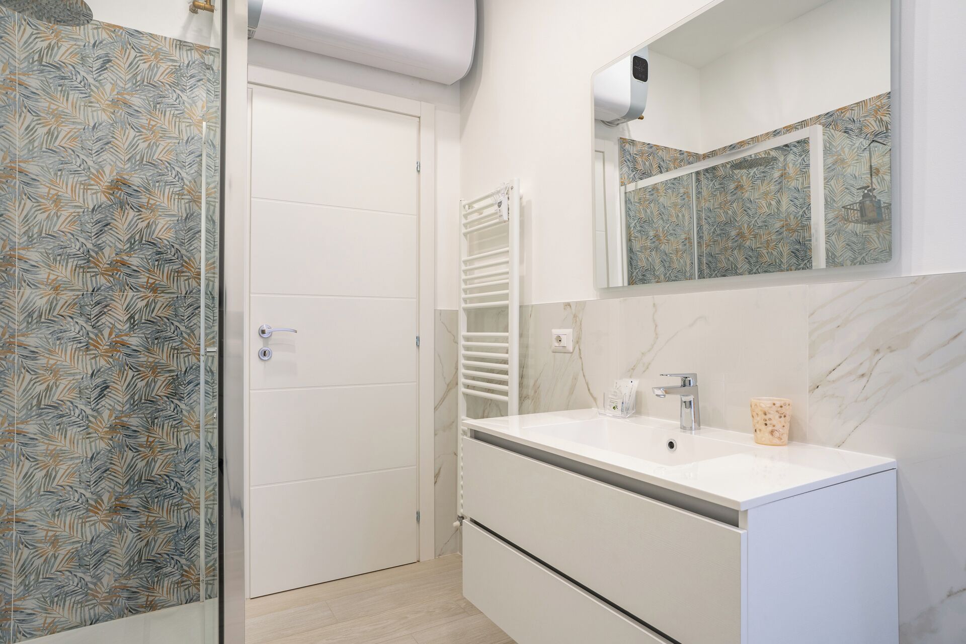 Un baño con tocador blanco, un espejo y zona de ducha con perchero blanco.