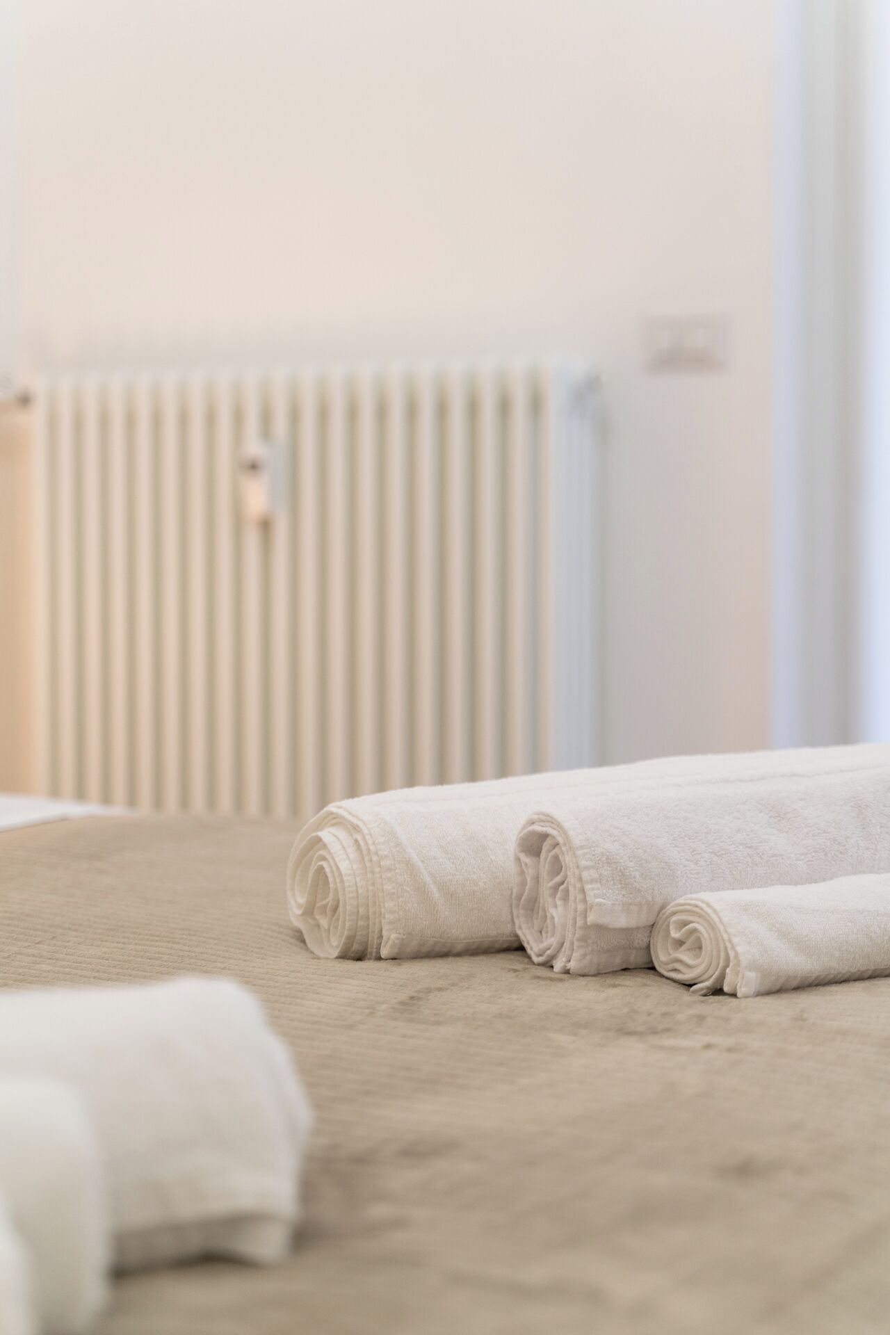 Un ensemble de serviettes blanches, soigneusement disposées, sur un tapis beige, dans une pièce où l’on aperçoit un radiateur à l’arrière-plan.