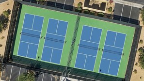 An aerial view of a tennis court complex with multiple courts, surrounded by a parking area and greenery.