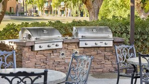 A patio with two stainless steel barbecue grills, stone walls, and wrought iron chairs.