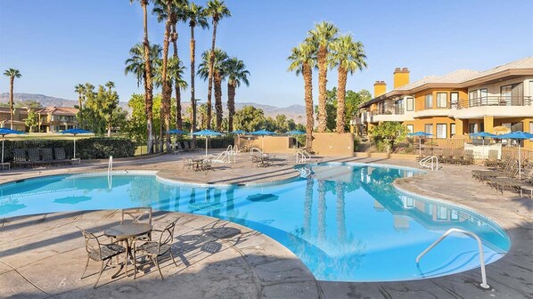 A pool area with lounge chairs, umbrellas, and palm trees.
