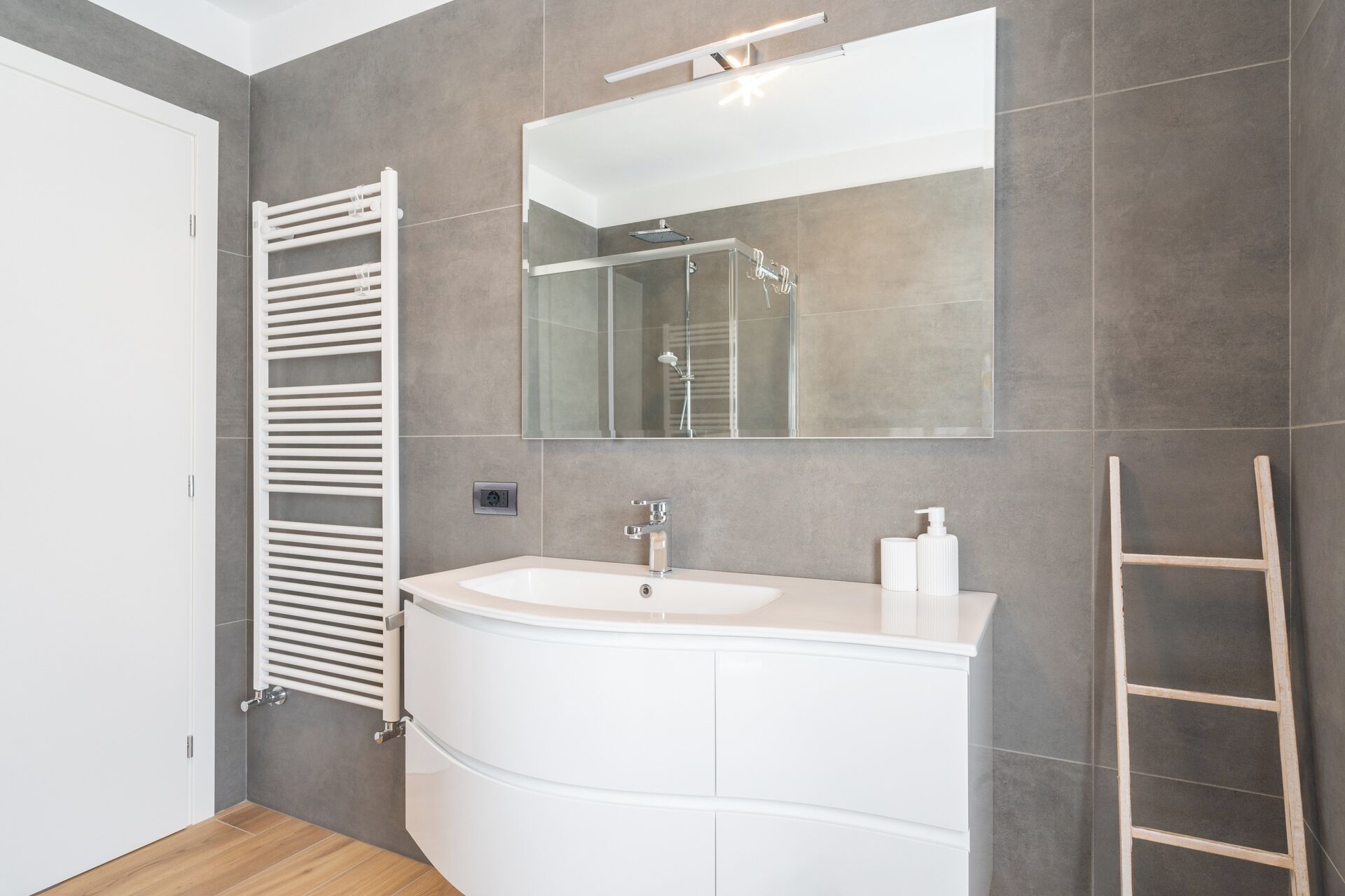 A modern bathroom with a white vanity, a glass shower enclosure, and a wooden ladder.