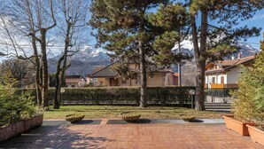 Un cortile lastricato con piante in vaso, una recinzione in metallo e case sullo sfondo, con vista su una montagna.