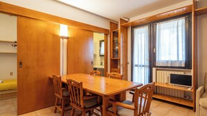 Zona pranzo con tavolo e sedie in legno, una libreria a muro e una finestra con tende.
