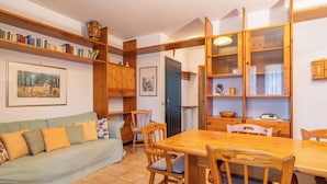 Un accogliente soggiorno con un tavolo da pranzo in legno, sedie, un divano con cuscini e mensole in legno con libri e oggetti decorativi.