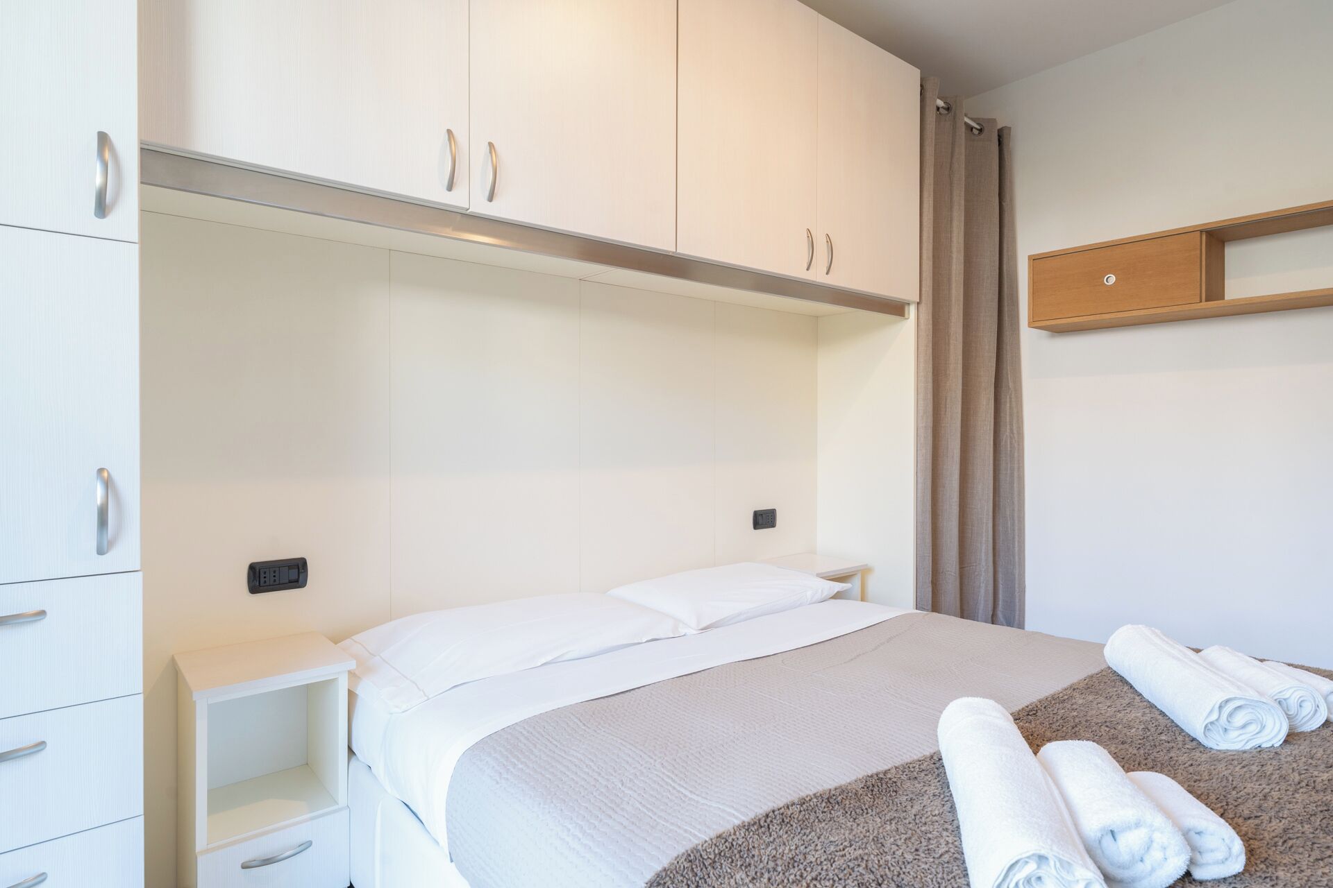 A hotel room with a bed, a nightstand, a wardrobe, and a towel rack.