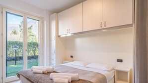 A bedroom with a bed, a nightstand, and a built-in wardrobe. There is a sliding glass door leading to a garden.