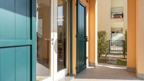 A building entrance with a glass door and a green door, leading to a tiled patio area.