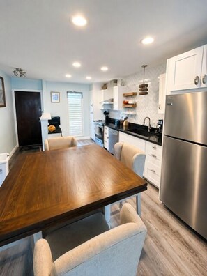Una cocina moderna con una mesa de comedor de madera, armarios blancos y electrodomésticos de acero inoxidable.