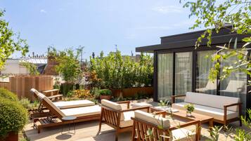 Une terrasse sur le toit, aménagée avec des fauteuils de jardin en bois, un canapé et une table.
