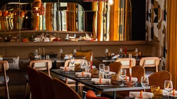 Un restaurante con una decoración moderna, con mesas largas dispuestas con copas de vino, platos y servilletas.