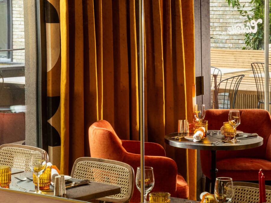 Ein Restaurantinnenraum mit einem Tisch für zwei Personen, mit Korbstühlen und einer roten, gepolsterten Couch.