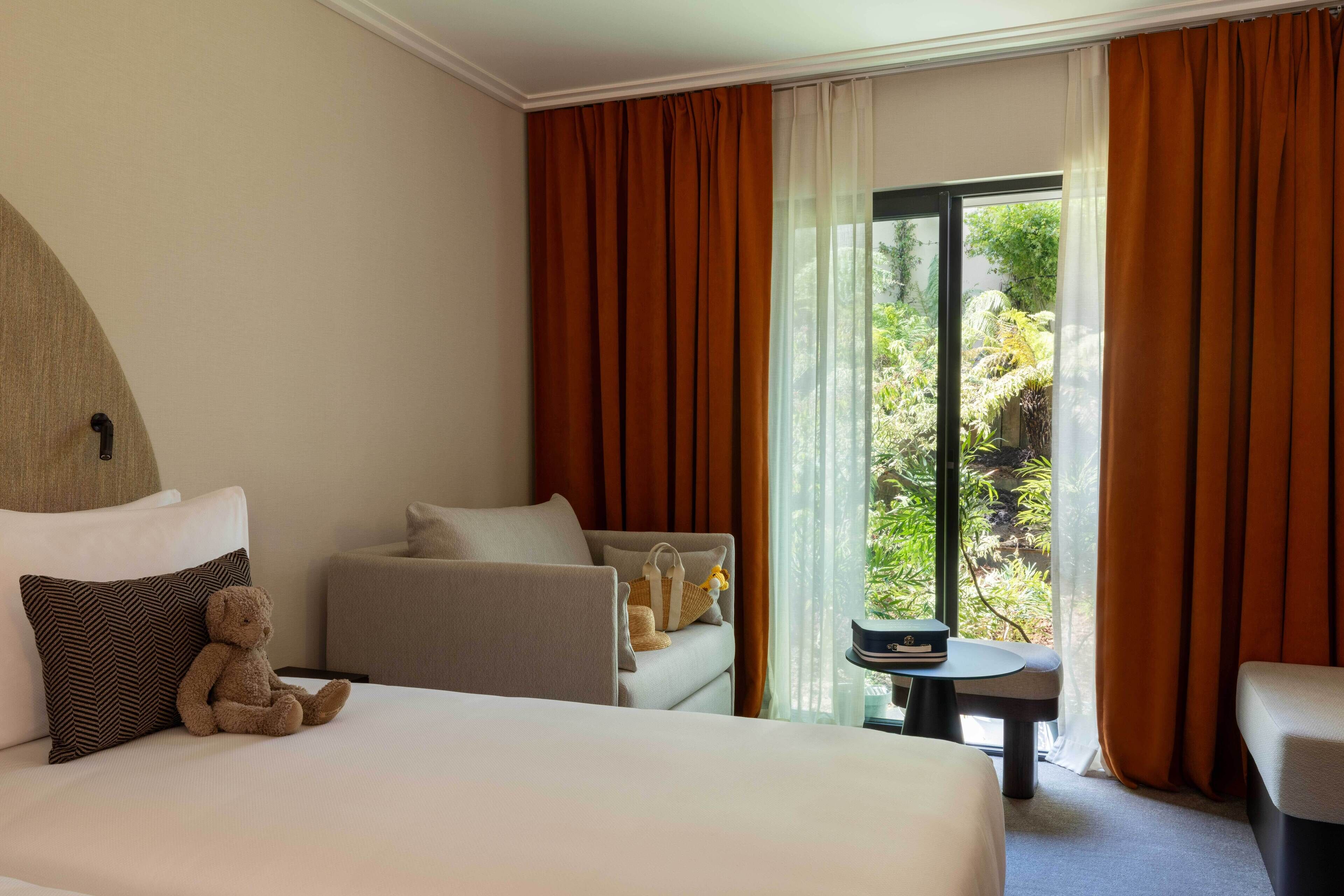 Une chambre d’hôtel avec un lit, un canapé, une chaise, une petite table et un ours en peluche.