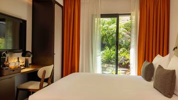 A hotel room with a bed, a desk with a lamp, a chair, and a TV.