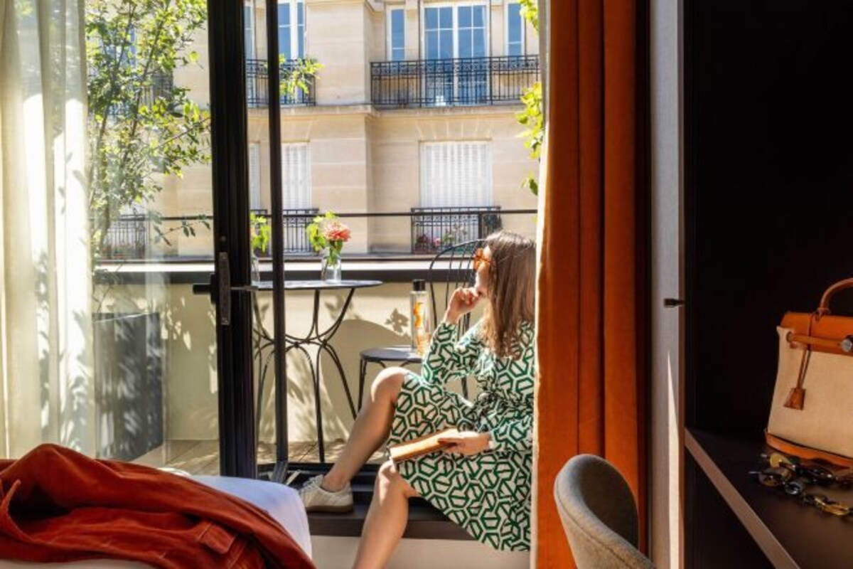 A room with a sliding glass door, a bed, a chair, and a table with a vase of flowers.